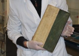 Un investigador sostiene (cuidadosamente) uno de los libros envenenados con arsénico. El tomo data del Renacimiento, pero es probable que haya sido cubierto con pintura de arsénico por los equivocados victorianos.
